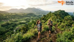 Travelers hiking through green Bali mountain trails with scenic valley and volcano views.