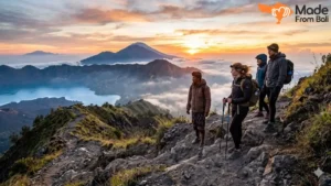 Hikers and local guide standing on Mount Batur trail during sunrise above clouds and volcanic landscape.