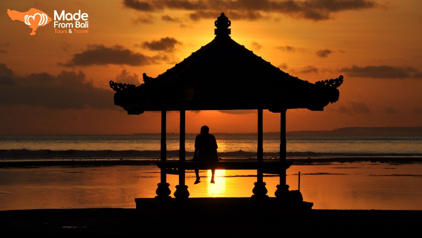 Person sitting in a beach pavilion, watching a colorful sunset over the ocean in Bali.