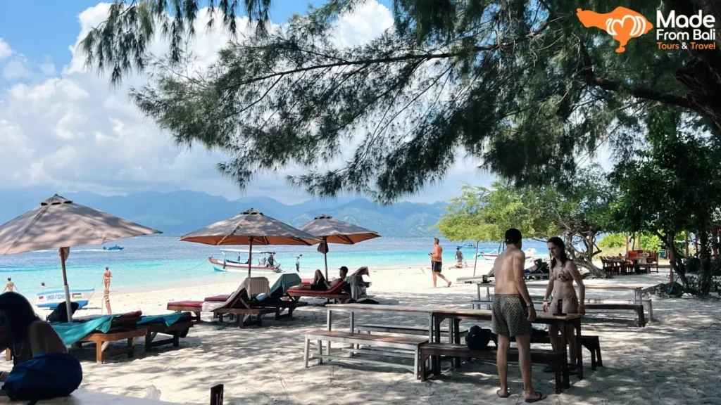 Visitors relax on a Gili Islands beach with clear water, showing a typical day trip from Bali.