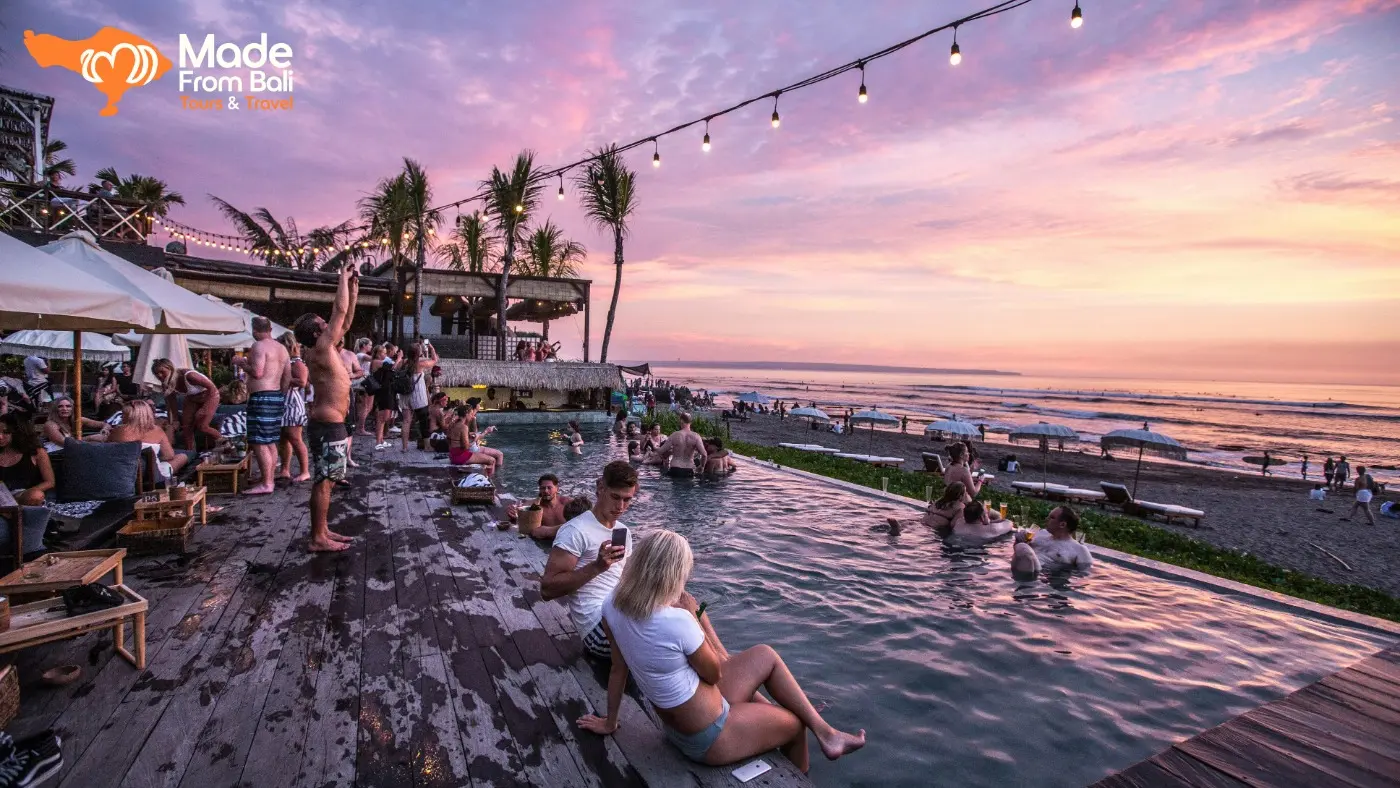 Guests relax in a beach club pool overlooking the ocean during sunset, showing Bali’s social beach club atmosphere