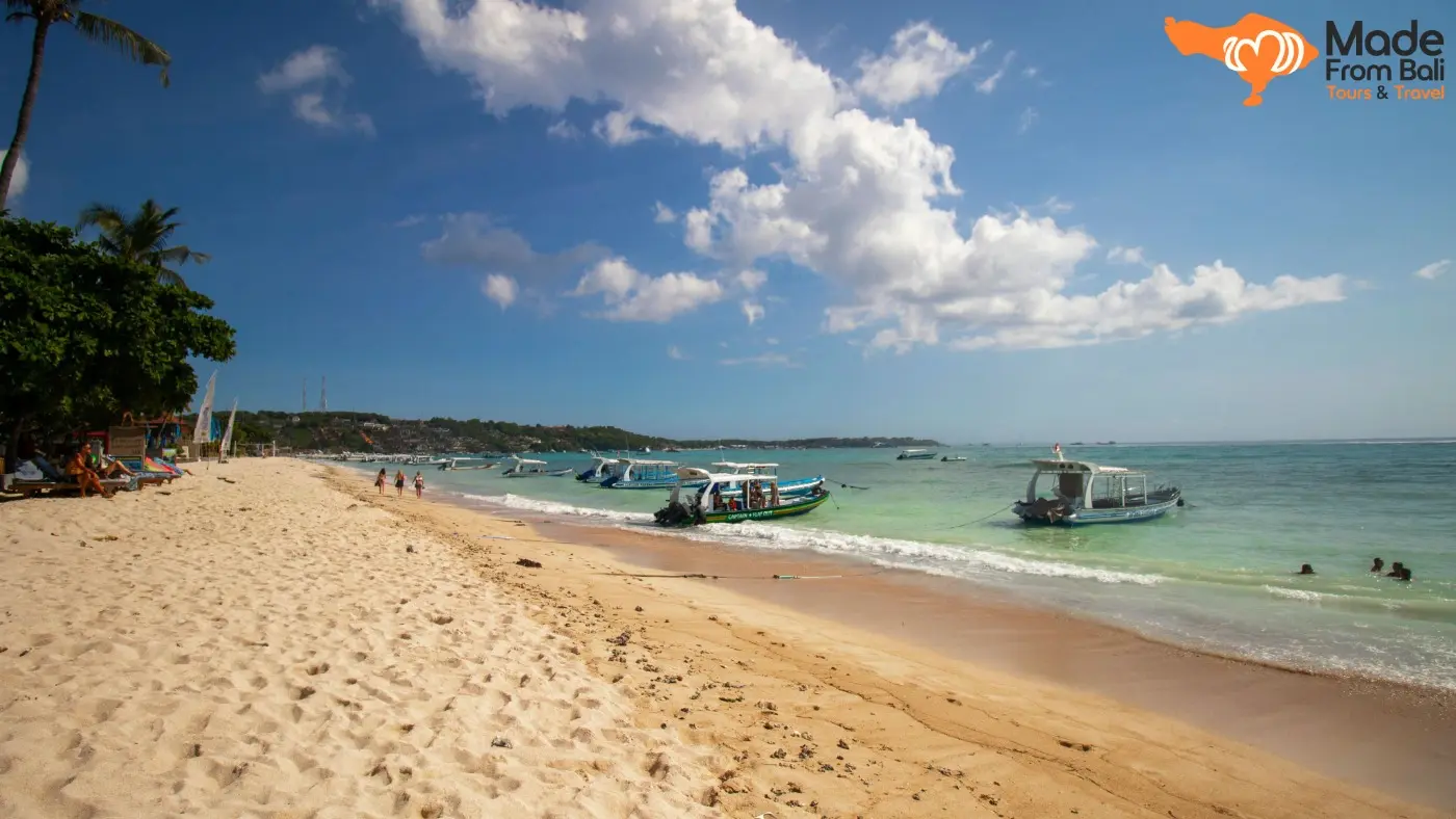 Pantai Nusa Lembongan dengan pasir putih, perahu wisata, dan air laut jernih di bawah langit cerah.